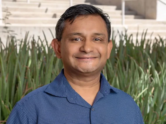 A photo of a man in a blue shirt with green plants behind him