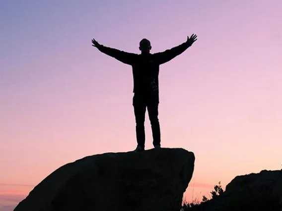 Man on top of rock with sunset behind him