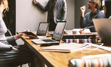 People sitting around a table in an office as a man presents.